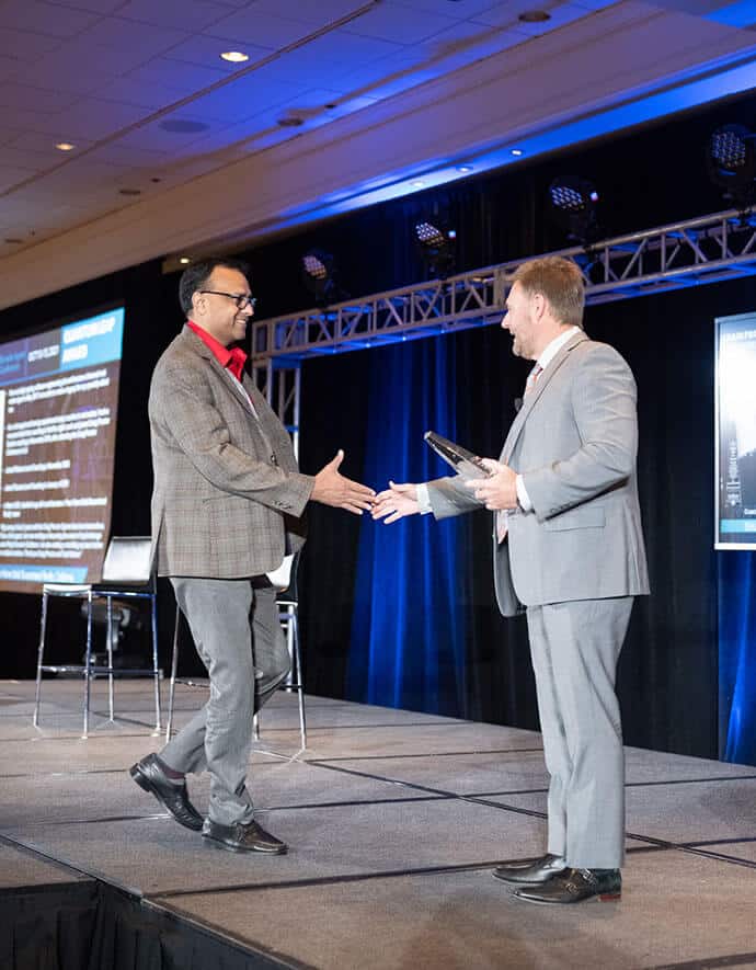 He accepts an award on stage, exchanging a handshake with the presenter at a professional conference.
