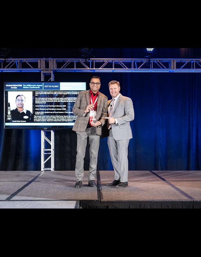 The Realtor receives an award from a colleague on stage, with a presentation in the background at a professional event.
