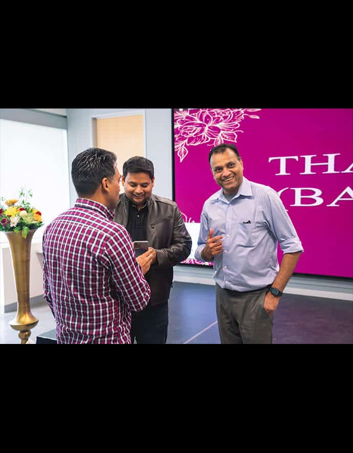 Sharad Gupta engaged in a lively discussion with two colleagues in front of a vibrant purple backdrop featuring a floral design.